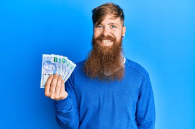 Genç İrlandalı kızıl saçlı adam Güney Afrika 'da elinde 100 rand banknot tutuyor. Pozitif ve mutlu görünüyor. Kendine güvenen bir gülümsemeyle dişlerini gösteriyor. 