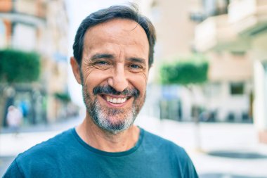 Orta yaşlı, sakallı, açık havada mutlu gülümseyen bir adam.