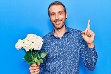 Elinde çiçeklerle gülümseyen genç yakışıklı bir adam bir fikirle ya da soru işareti yaparak mutlu bir yüzle, bir numara 