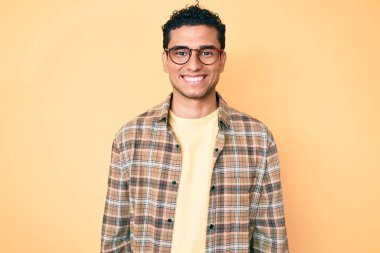 Genç, yakışıklı İspanyol bir adam günlük kıyafetler ve gözlük takıyor. Pozitif ve mutlu görünüyor. Kendine güvenen bir gülümsemeyle dişlerini gösteriyor. 