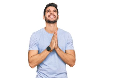 Gündelik giysiler giyen genç İspanyol adam elleri bağlı yalvarıyor ve dua ediyor. Yüzünde umut ifadesi var. Çok duygusal ve endişeli. Yalvarıyor. 