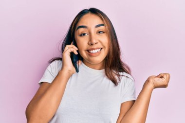 Genç Latin kadın telefonda konuşuyor gururla bağırıyor, zaferi kutluyor ve kollarını kaldırarak heyecanlanıyor. 