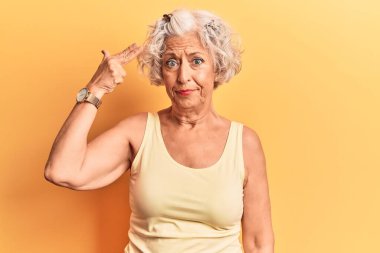 Kıdemli gri saçlı kadın, günlük giysiler giymiş, silah gibi elini ve parmaklarını havaya kaldırarak ateş ediyor, kendini öldürüyor.. 