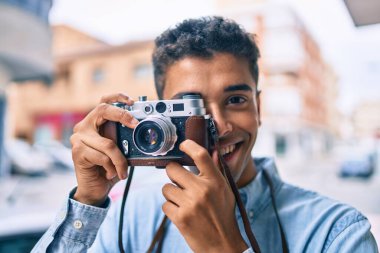 Genç Latin turist mutlu bir şekilde gülümsüyor. Şehirde eski model kamera kullanıyor..