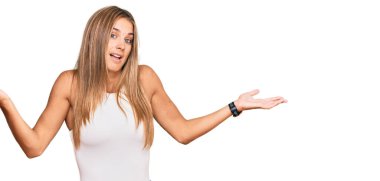 Kolsuz tişörtsüz, kolları ve elleri havada, kafası karışmış genç sarışın kadın. şüphe kavramı. 