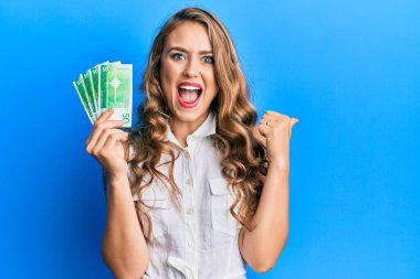 Norveç kronu banknotları tutan genç sarışın kız başparmağıyla yan tarafı işaret ediyor ve ağzı açık gülümsüyor. 