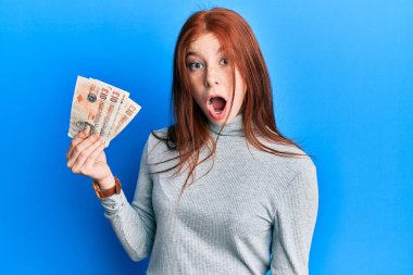 Genç kızıl saçlı kız elinde 10 pound tutuyor. Banknotlar korkmuş ve hayrete düşmüş. Şaşırtıcı bir şekilde ağzı açık. 
