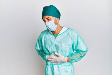 Genç yakışıklı bir adam cerrah üniforması giyiyor ve elleri karnında tıbbi maske takıyor çünkü mide bulantısı, acı verici bir hastalık kendini iyi hissetmiyor. Ağrı kavramı. 