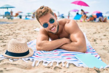 Güneşli bir günde kumsalda havluyla güneşlenen yakışıklı beyaz adam.