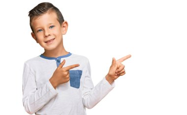 Gündelik kıyafetler giyen sevimli beyaz çocuk gülümseyip kameraya bakıyor ve iki eliyle ve parmaklarıyla kenarı işaret ediyor.. 