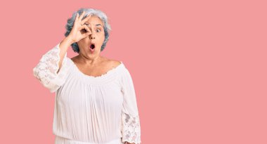 Gri saçlı, bohem tarzı giyinen yaşlı bir kadın. Şaşırmış bir yüz ve parmaklarından bakan bir gözle şok olmuş bir jest yapıyor. İnançsız ifade. 