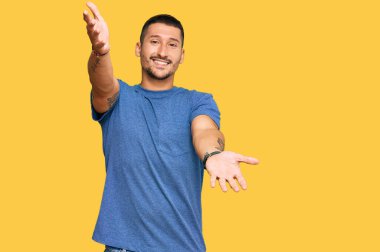 Sıradan kıyafetler giyen yakışıklı bir adam kucak açmak için kollarını açmış kameraya bakıyor. Mutluluğu kucaklayan neşeli bir ifade.. 