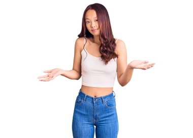 Gündelik kıyafetler giyen genç, güzel Çinli bir kız. Kolları ve elleri havada, kafası karışmış bir ifade. şüphe kavramı. 