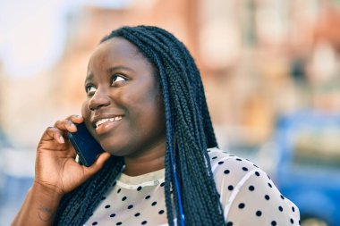 Genç Afrikalı Amerikalı kadın gülümsüyor. Şehirdeki akıllı telefondan mutlu bir şekilde konuşuyor..