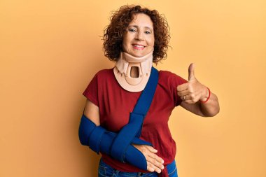 Güzel orta yaşlı olgun bir kadın, boyun tasması takıyor ve kolu askıda gülümsüyor, mutlu ve pozitif, başparmağıyla mükemmel ve onay işareti yapıyor. 