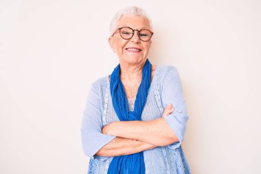 Mavi gözlü, gri saçlı, sıradan süveter giyen ve kollarını kavuşturup kameraya bakan mutlu yüzlü son sınıf güzeli bir kadın. pozitif kişi. 