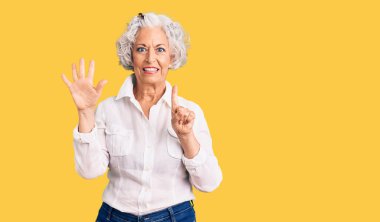 Kıdemli, gri saçlı, günlük kıyafetler giyen, altı numaralı parmaklarıyla işaret eden, kendinden emin ve mutlu bir kadın.. 