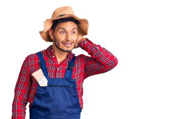 Yakışıklı Latin Amerikalı, giyimli, tamirci üniforması giyen, kendine güvenen, el hareketleriyle saçlarına dokunan, çekici ve modaya uygun poz veren genç adam. 
