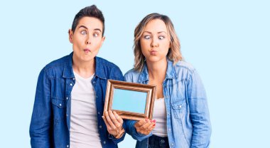 Elinde boş bir çerçeve olan iki kadın dudaklarıyla balık suratı yapıyor, çılgınca ve komik bir jest. Komik ifade. 