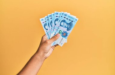 Çin malı 10 Yuan 'lık banknotları izole edilmiş sarı arka planda tutan İspanyol adamın eli..