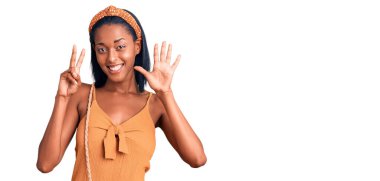 Genç Afro-Amerikalı kadın yaz kıyafeti giyip yedi numarayı gösterip işaret ederken kendinden emin ve mutlu bir şekilde gülümsüyor.. 