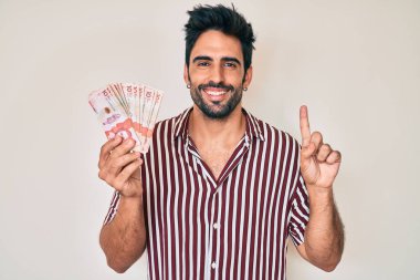 Sakallı yakışıklı İspanyol bir adam elinde bir fikirle gülümseyen Kolombiya pezosu ya da mutlu yüzle işaret eden soru işareti yapan bir numara. 