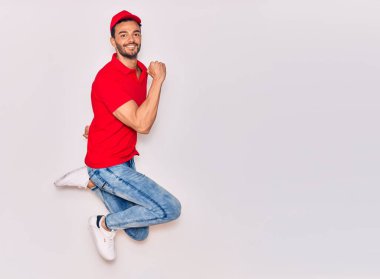 Mutlu gülümseyen üniformalı yakışıklı İspanyol teslimatçı. Yüzünde tebessümle zıplıyor, beyaz arka planda yumruklar havada kutluyor..