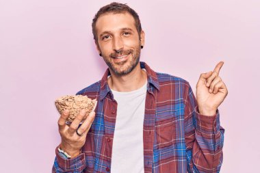 Genç yakışıklı adam elinde mısır gevreği tutarken gülümsüyor. 