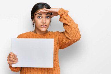 Elinde boş afiş tutan genç esmer kadın elleri kafasında, şaşırmış ve sinirli yüzüyle stresli ve hayal kırıklığına uğramış. 