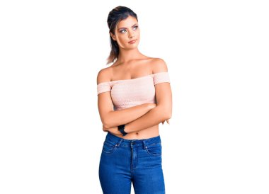 Genç ve güzel bir kadın, sıradan kıyafetler giyip kollarını kavuşturmuş ve kendinden emin bir şekilde yan tarafa bakıyor. 