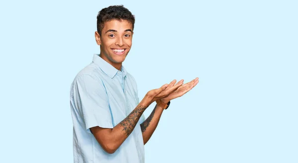 若いですハンサムなアフリカ系アメリカ人男性を身に着けていますカジュアル服を指して脇に手を開いてヤシの木を示しますコピースペース 提示広告笑顔興奮幸せ — ストック写真