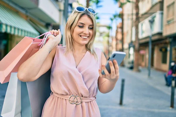 Genç Sarışın Kadın Gülümsüyor Alışveriş Torbaları Tutuyor Şehirde Akıllı Telefon — Stok fotoğraf