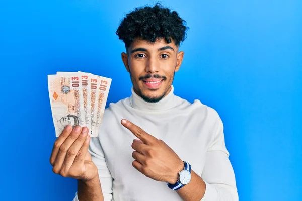 年轻的Arab英俊男子 手里拿着10英镑的英国钞票 高兴地微笑着 手指手画脚 — 图库照片