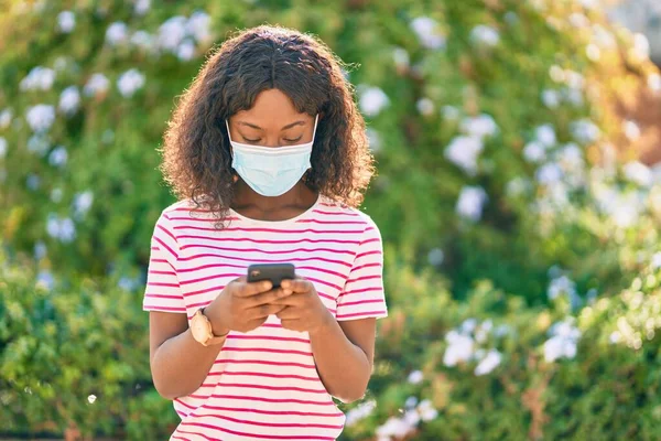 Νεαρή Αφροαμερικανή Που Φοράει Ιατρική Μάσκα Χρησιμοποιώντας Smartphone Στο Πάρκο — Φωτογραφία Αρχείου