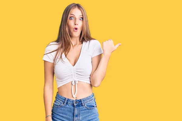 Young Beautiful Blonde Woman Wearing Casual White Tshirt Surprised Pointing — Stock Photo, Image