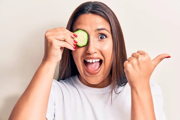 Young Beautiful Brunette Woman Holding Slice Cucumber Pointing Thumb Side — ストック写真