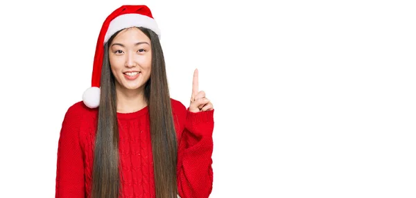 若いです中国人女性身に着けているクリスマスの帽子ショーとポイントアップとともに指第1位ながら笑顔自信と幸せ — ストック写真