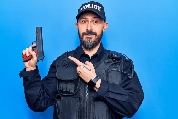 Mladý Pohledný Muž Policejní Uniformě Drží Zbraň Úsměvem Šťastný Ukazuje — Stock fotografie