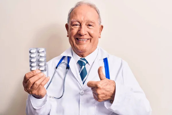 Starszy Siwowłosy Lekarz Noszący Stetoskop Trzymający Tabletki Białym Tle Uśmiechający — Zdjęcie stockowe