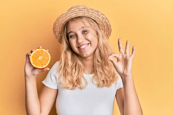 穿着夏装的金发女郎拿着一片橙子 手拿着手签 微笑着表示友善的手势 象征着极好的象征 — 图库照片