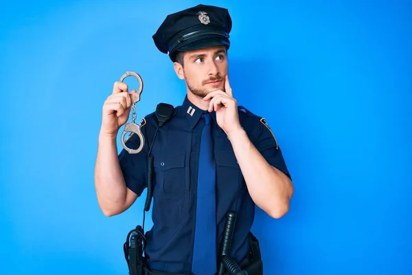 Joven Hombre Caucásico Vistiendo Uniforme Policía Sosteniendo Esposas Cara Seria —  Fotos de Stock