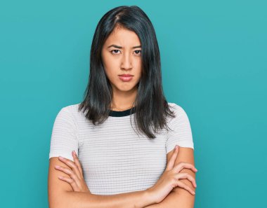 Güzel Asyalı genç bir kadın sıradan beyaz tişörtler giyiyor şüpheci ve gergin, yüzünde çapraz kollarla onaylamayan bir ifade var. negatif kişi. 