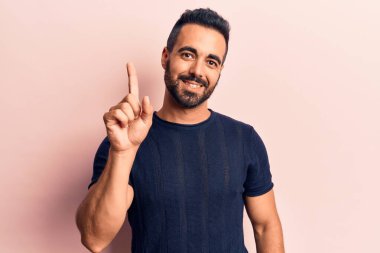 Bir fikir veya soruyla gülümseyen gündelik kıyafetler giyen genç İspanyol adam, bir numara, mutlu bir yüzle işaret ediyor. 