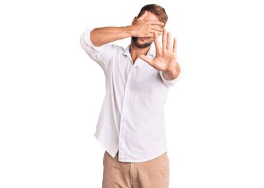 Kafkasyalı genç bir adam günlük kıyafetler giyip elleriyle gözlerini kapatıyor ve üzgün ve korku ifadeleriyle jestleri durduruyor. utangaç ve olumsuz kavram. 