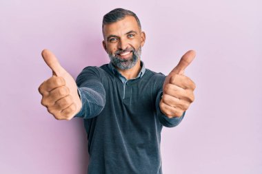 Orta yaşlı yakışıklı bir adam günlük kıyafetlerini giyiyor. Elleriyle olumlu bir jest yapıyor. Gülümsüyor ve başarı için seviniyor. kazanan jest. 