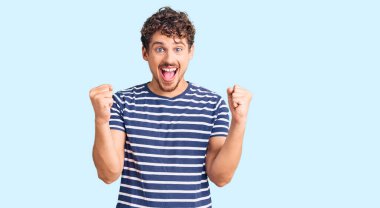 Kıvırcık saçlı, gündelik giysiler giyen genç yakışıklı adam kollarını kaldırıp açık gözlerle başarıyı kutluyor ve şaşırıyor. Kazanan konsept. 