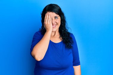 Artı, mavi günlük gömlek giyen esmer kadın bir gözünü eliyle kapatıyor, yüzünde kendine güvenen bir gülümseme ve sürpriz bir duygu var.. 