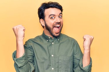 Gündelik kıyafetler giyen genç İspanyol adam gururla bağırıyor, zaferi ve başarıyı kutluyor. Kollarını kaldırarak heyecanla bekliyor. 