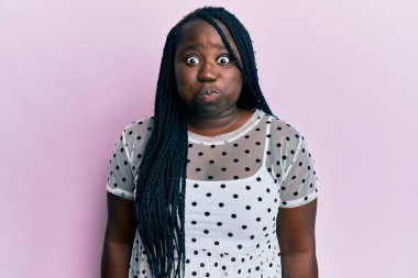 Saçları örgülü, sıradan kıyafetler giyen, komik yüzlü, yanak şişiren genç siyahi bir kadın. Havayla şişmiş ağız, çılgın bir ifade.. 