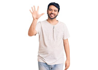 Gündelik kıyafetler giyen genç İspanyol adam beş numarayı gösterip işaret ederken kendinden emin ve mutlu bir şekilde gülümsüyor.. 
